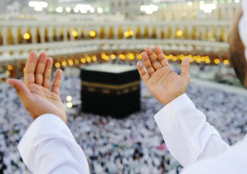 Pilgrim raising hands in dua before the Kaaba